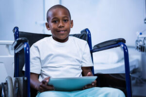 Portrait of boy sitting on wheelchair with digital tablet in ward at hospital